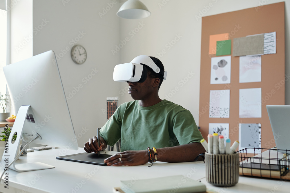 Aufkleber Young graphic designer in extended reality headset using stylus and touchpad while creating new computer games by workplace