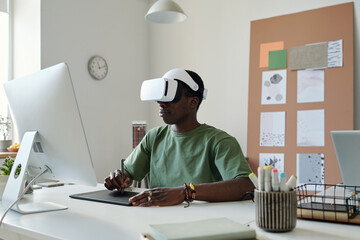 Young graphic designer in extended reality headset using stylus and touchpad while creating new...