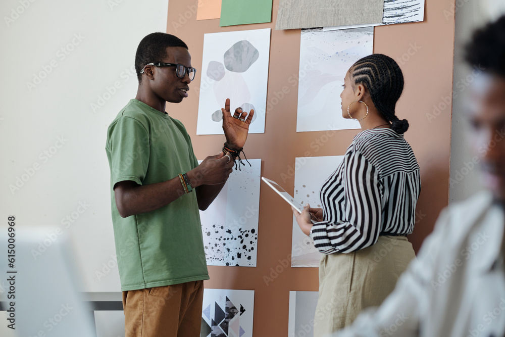 Poster confident male designer or architext explaining something to female colleague by noticeboard with gr