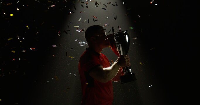 Silhouette of Caucasian male rugby player raising a trophy above head against bright light and falling confetti. Super slow motion, shot on RED cinema camera