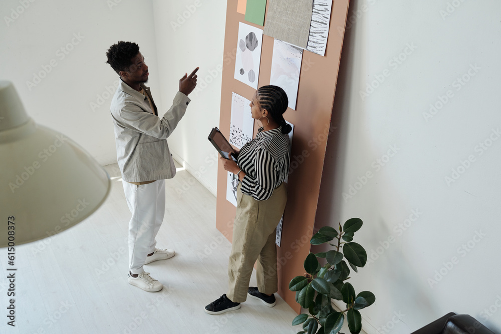 Poster young confident businessman pointing at one of papers with graphic drawings on noticeboard while exp