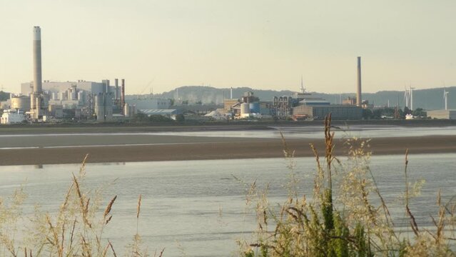 Looking across river Mersey estuary to Runcorn industrial waterfront factory businesses at sunrise low tide