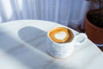 Hot coffee latte with latte art milk foam in white stone patterned cup mug on wood desk on top view. As breakfast In a coffee shop at the cafe,during business work concept
