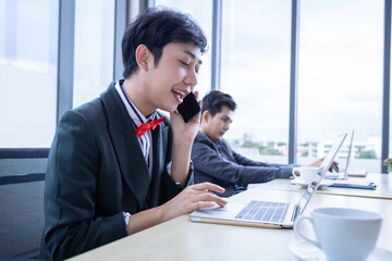 Homosexual Asian businessman LGBT talking with mobile phone while working at laptop computer and business people group in the meeting room at modern office