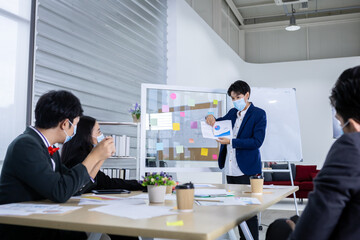 asian female coach Wear protective mask speaker make flip chart presentation to diverse business people meeting with diverse genders (LGBT) in the room at office,COVID-19
