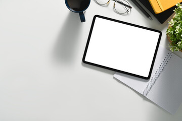 Top view of modern workplace with digital tablet, coffee cup, glasses and notepad on white working desk