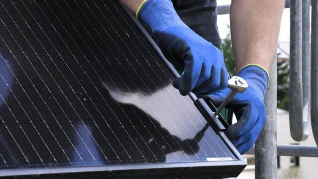 Close-up view of a technician's hands installing a solar panel on the roof of a house