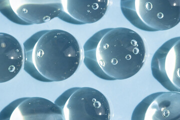 Transparent drops of serum on a blue background, top view. Beauty background with liquid care...