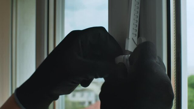 Close-up of a man's hand in a construction glove fixing a plastic window opening stopper. Installing a window stopper on a plastic window frame. Accessories of plastic windows. Modern window frames