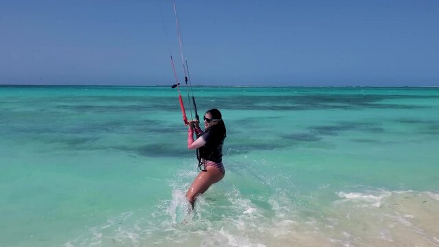 Hispanic woman rookie kitesurfer  use bar control on shoreline beach while wind raise her