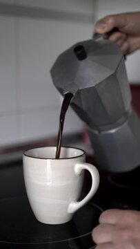 Anonymous person pouring coffee from his Italian coffee maker into his cup. Vertical shot of an unrecognizable man's hands preparing a fresh coffee in his kitchen.