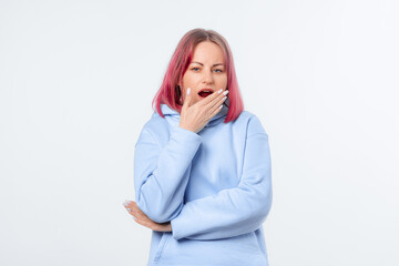 Sleepy woman yawn with tired face. Night Owl type concept. Lovely female model with pink hair in a blue hoodie standing over white background