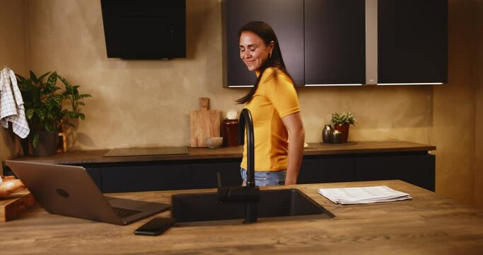 Smiling young woman dancing to music from a laptop in her kitchen at home