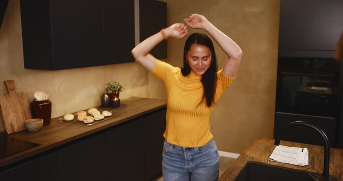 Smiling young woman working online on a laptop and dancing in her kitchen at home