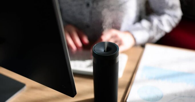 Air humidifier device on office table closeup. Female manager using essential oil diffuser while sitting at working desk