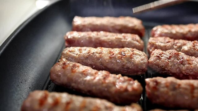 Grilling meat on a grill pan. Smoking sausages are turned over with tongs. Food preparation. Chevapi Traditional Balkan grilled sausages. Close up. High quality footage
