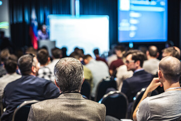 Speaker giving a talk in conference hall at business event. Rear view of unrecognizable people in audience at the conference hall. Business and entrepreneurship concept