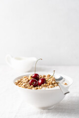 Bowl of homemade granola with nuts and cherry in white bowl on light background. Quick healthy breakfast