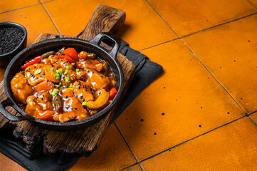 Chinese Sweet and sour chicken with colorful bell pepper in a skillet. Orange background. Top view....