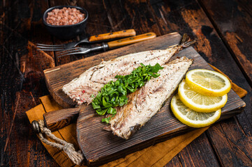 Delicious baked mackerel fillets with greens, garlic and lemon on wooden board. Wooden background. Top view - obrazy, fototapety, plakaty