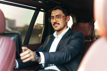 Young elegant businessman watching TV on the screen in luxury car