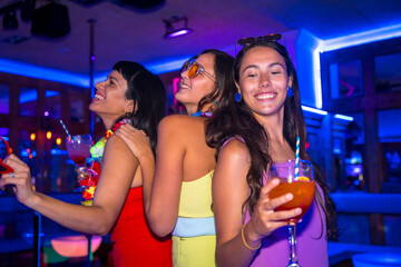 Female friends in a nightclub drinking glasses of alcohol smiling at a night party