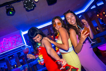 Female friends in a nightclub dancing with glasses of alcohol smiling at a night party