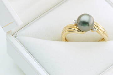 Gold ring with grey pearl and small diamonds in white jewelry box close up with copy space