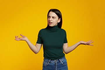 Uncertain confused girl expressing doubts and bewilderment, looking away with question so what, who cares, isolated over yellow background