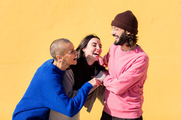 group of three friends laughing and joking around on yellow background, concept of friendship and...