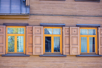 
A house of brown grass horizontal boards with three window sashes and a slangierm in orange color