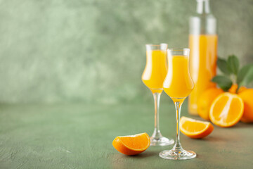 Arancello in grappas wineglass, sweet Italian orange liqueur, traditional strong alcoholic drink and oranges on the green wooden background. Copy space - obrazy, fototapety, plakaty