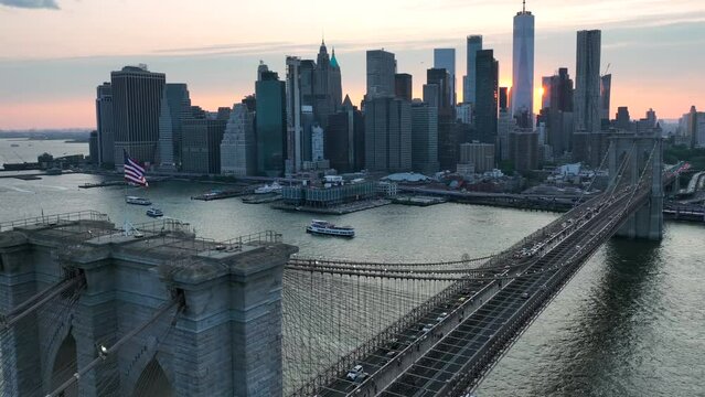 Lower Manhattan, financial district in NYC, during golden hour sunset. Aerial view from Brooklyn Bridge with American flag waving.