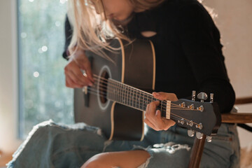 Music and hobbies. A talented young musician girl sits alone and composes songs on the guitar. The...