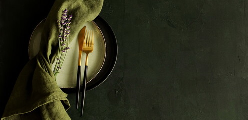 kitchen tableware, green linen napkins ,cutlery  and lavender flowers top view on dark green background banner. Space for text. Business food brand template. 