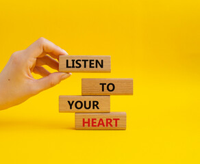 Listen to your heart symbol. Concept word Listen to your heart on wooden blocks. Beautiful yellow background. Businessman hand. Business and Listen to your heart concept. Copy space