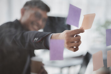 Businessman looking at post-it notes on mirror, he looks at data after a meeting between executives and department employees to discuss and grow the company. Management concept of a startup company.