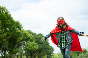 On a beautiful day in the park, a young girl enjoys her vacation. Playful with a red superhero costume and mask.