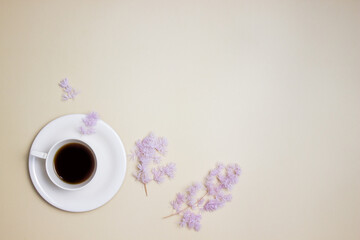 A cup of coffee with purple flower over the cream background with copy space.