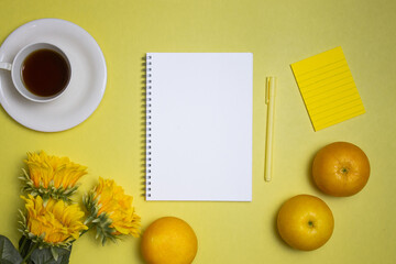 Office items with notebook, coffee, oranges, and flowers over the yellow background. 