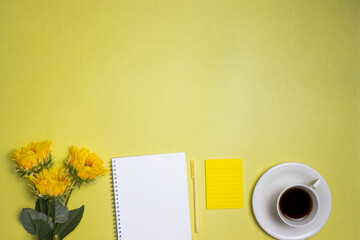 Yellow concept with notebook, flowers and a cup of coffee over the yellow background.