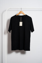 Black t-shirt mockup with blank price tag on wooden hanger hanging on a clothes rack