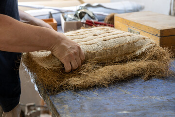 Upholstery craftsman shapes a pack filled with plant fibers like coir or palm fiber for a seat or...