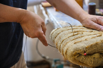 Upholstery craftsman sews a molded pack filled with coir (coconut fiber) with a curved needle to...