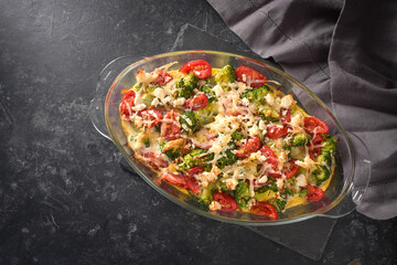 Casserole from broccoli, tomatoes, onions, feta and cheese, healthy vegetable dish on a dark gray...