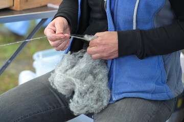 Hands of a woman spinning raw gray wool into thread at a craft market, selected focus