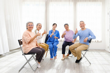 Fototapeta premium The caregiver therapist sits with a group of Asian senior people with thumbs up in a circle for checking physical and mental health in a group elderly therapy session. The nursing home facilitates