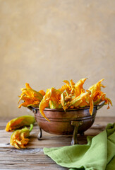 Zucchini flowers in a brass colander with green napkin. Vertical shot, wooden table, copy space for text