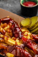 French fries baked with cheddar cheese, pickle and sausages in a paper plate on a dark background, Fast food take away. Top view, copy space