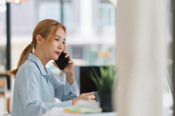 Obraz premium Young adult Asian businesswoman, secretary, sales manager, business consultant, engaging in a phone conversation with a client at the office.
